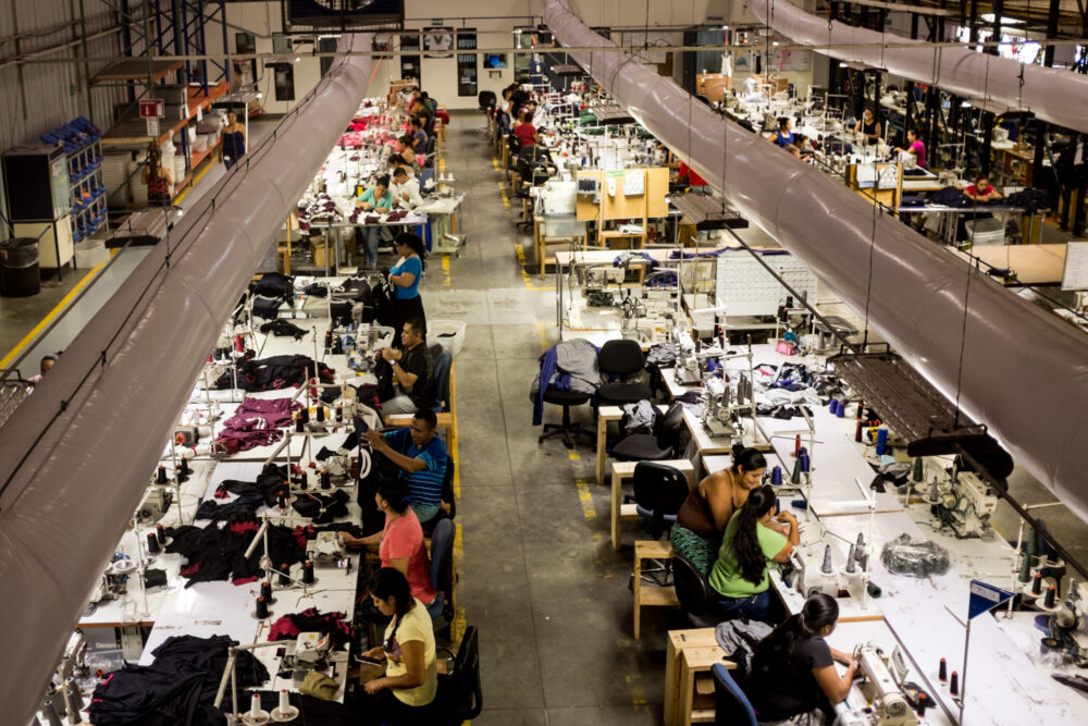 A factory floor is shot from above; dozens of workers are sewing